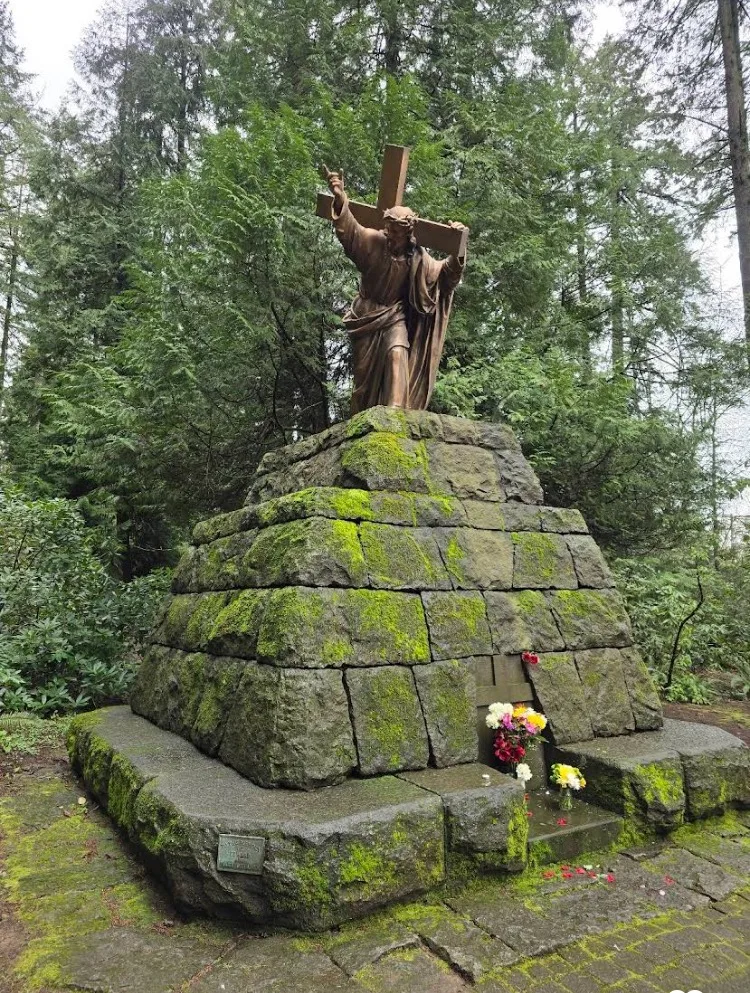 Bronze statue with cross on moss-covered stone at The Grotto